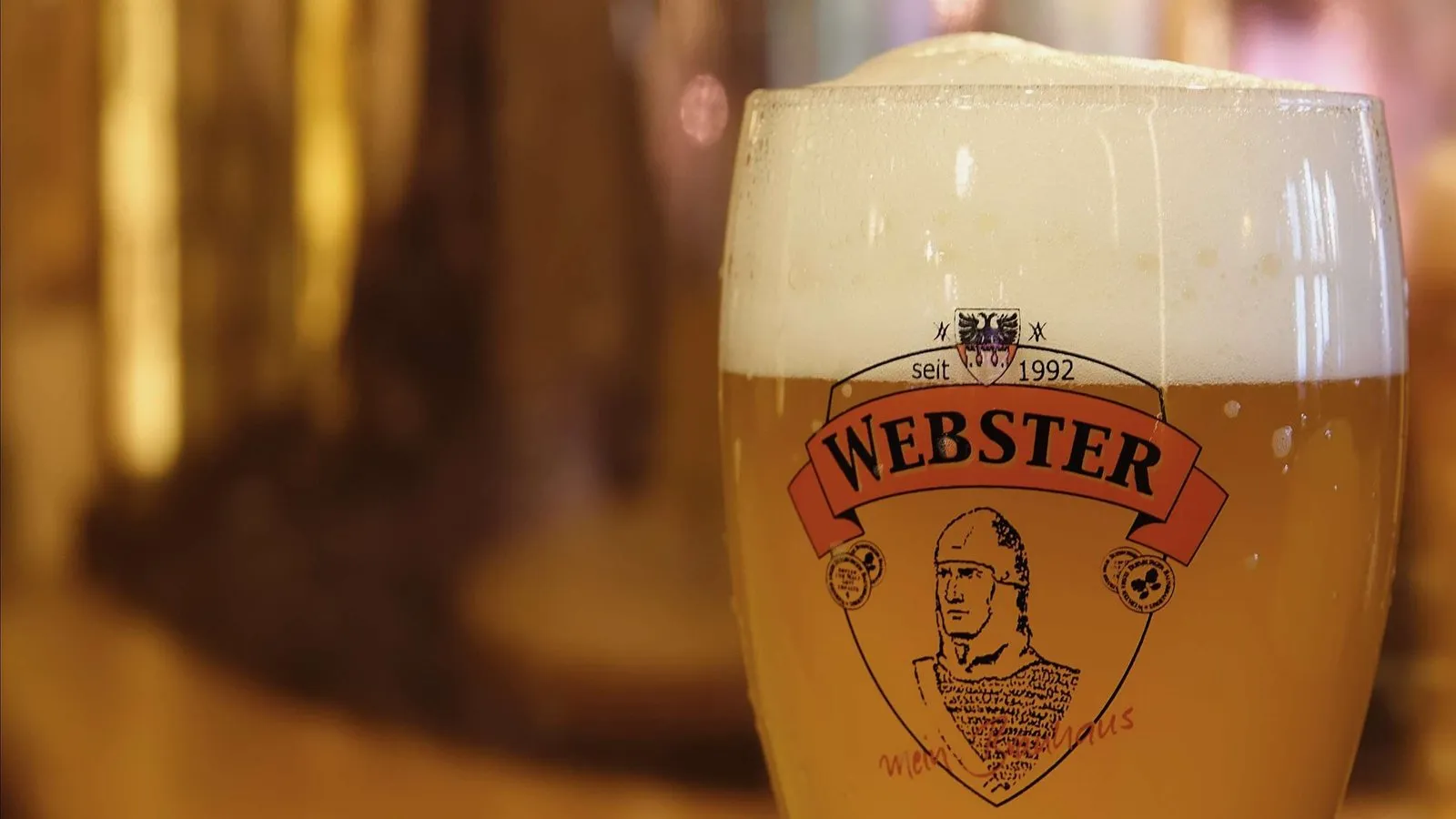 Frisch gezapftes Webster Bier im Glas mit dem Wappen der Brauerei